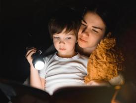 Woman and child reading in the dark with a flashlight
